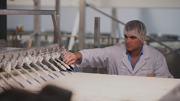 Mann mit Haarnetz und weißem Kittel bedient eine Maschine in einer Produktionshalle