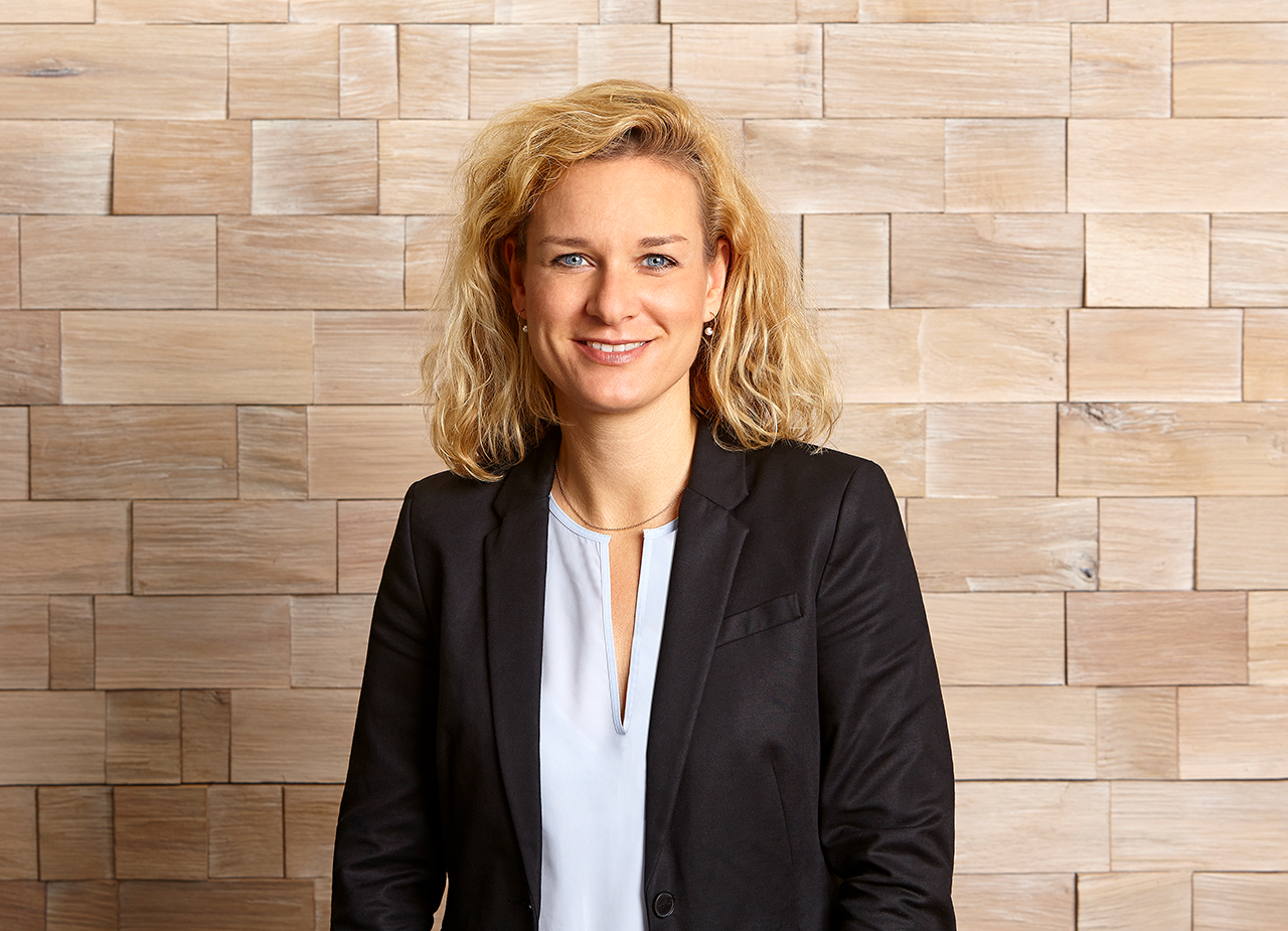 Simone Seidel, lächelnde blonde Frau mit heller Bluse vor einem Fenster