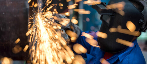 Eine Person mit Schweißhelm schweißt Metall, Funken sprühen
