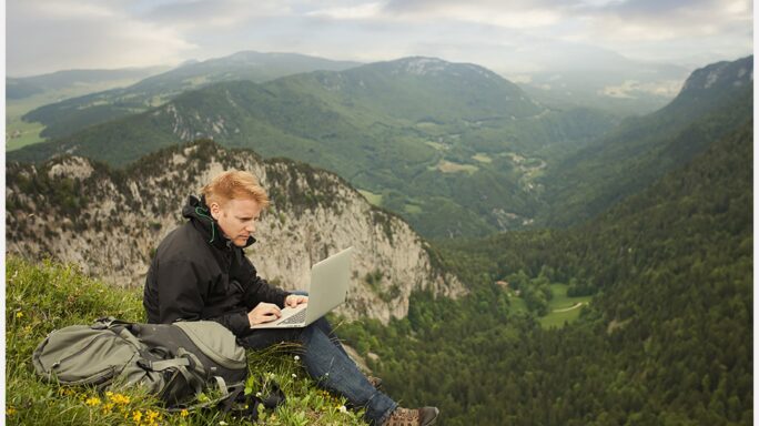 Caucasian man using laptop on remote cliff's edge