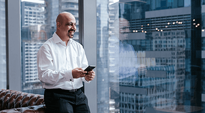 Man in high-rise office with smartphone, beaming