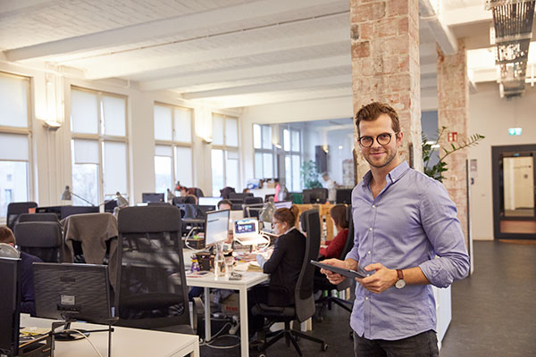 a man standing in an open office space holding a tablet