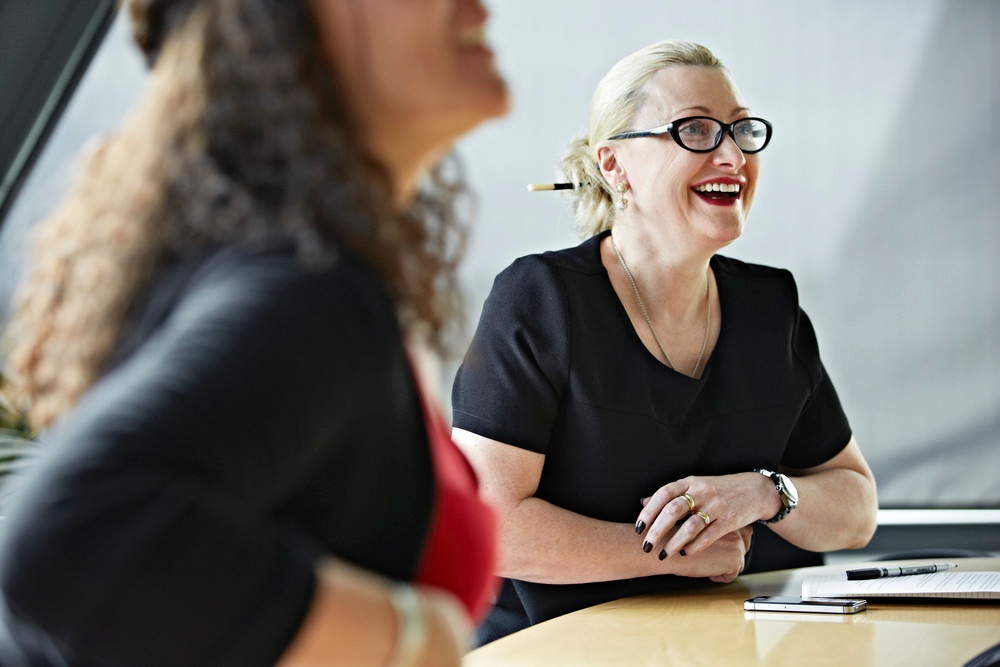 Two colleagues laughing while sitting at a boardroom table