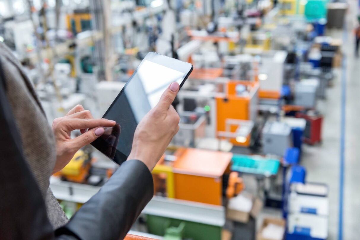 a manager holds an ipad and overlooks a factory and warehouse floor