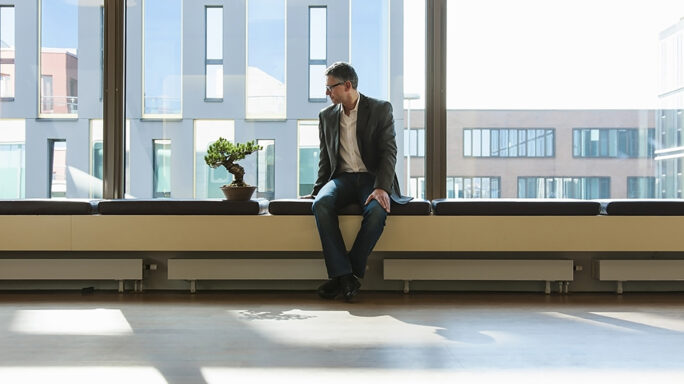 Businessman sitting on a window seat in a high rise office building looking out the window