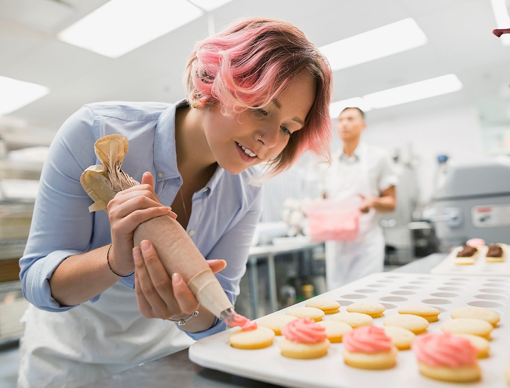 Pastry chef piping cookies with pink icing in a commercial kitchen