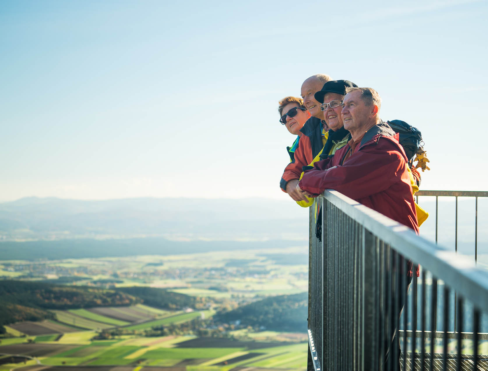 four middle aged people look out at a high view from behind a railing