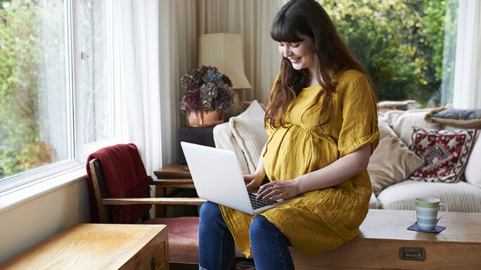 Pregnant woman smiling while using laptop at home