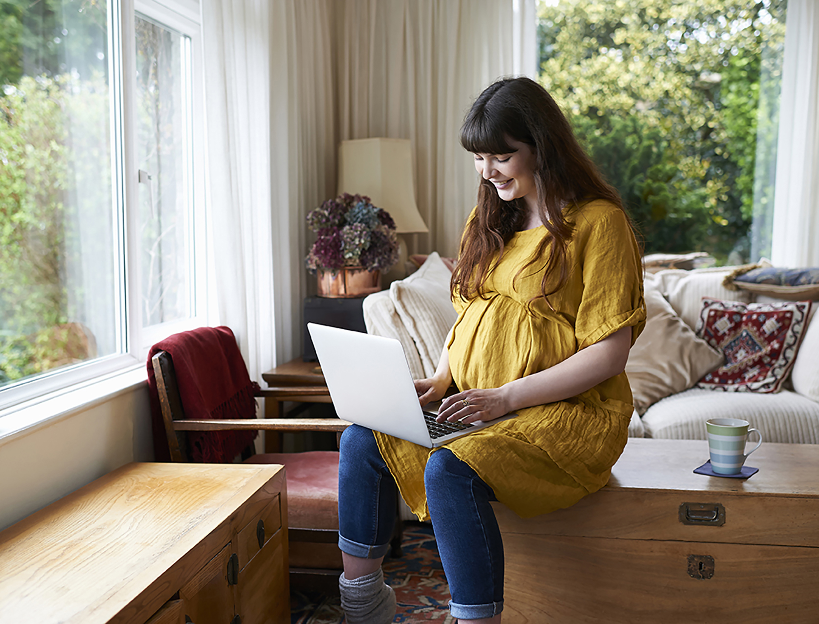 Pregnant woman smiling while using laptop at home