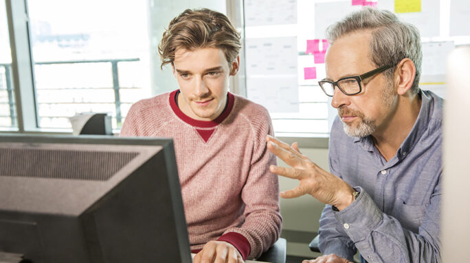 project manager talks to designer while looking at computer