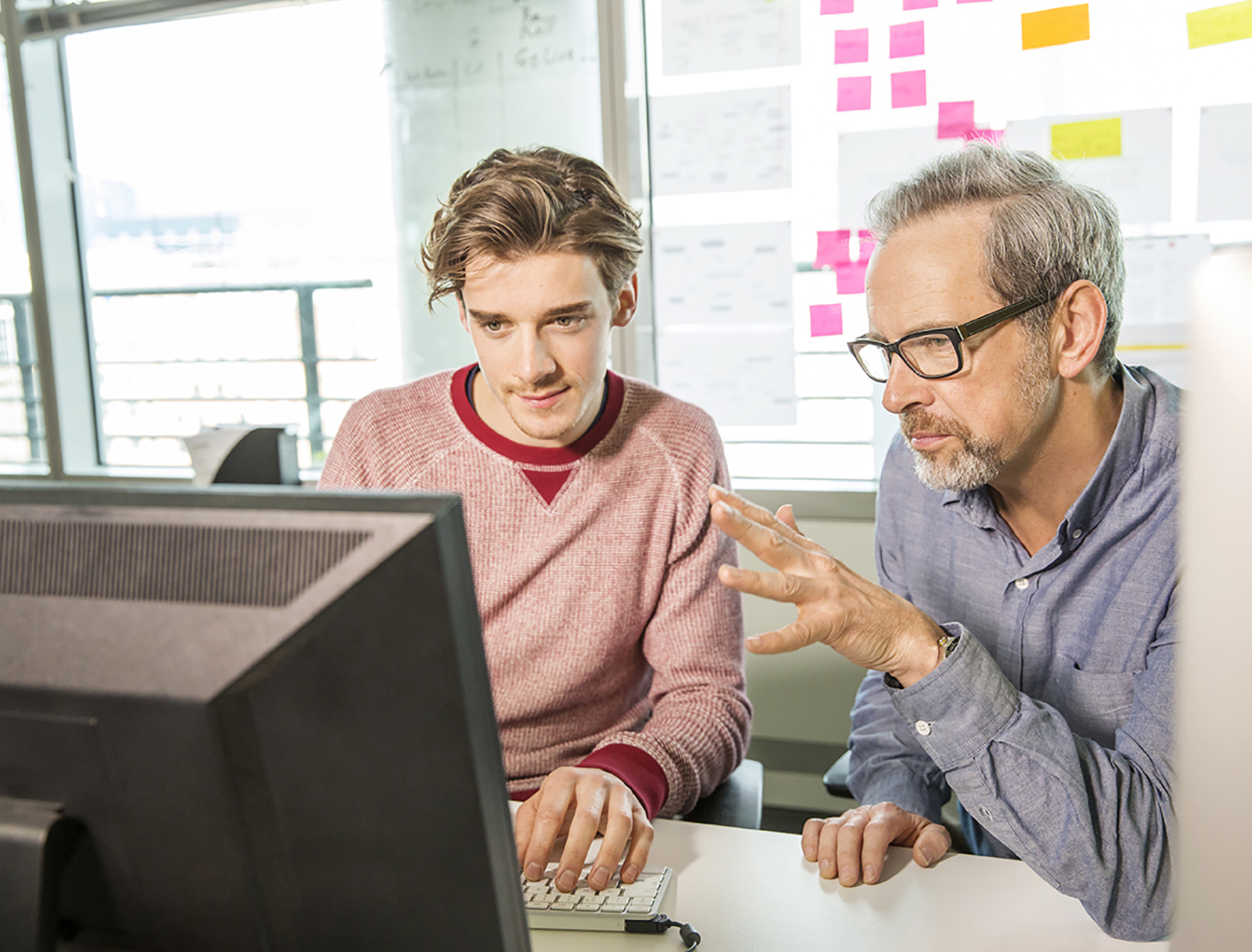 project manager talks to designer while looking at computer