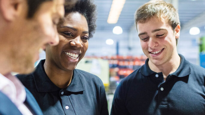 three team members smile with each other in the middle of a warehouse foor
