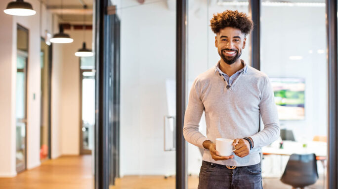 man holds coffee cup in the middle of a modern open plan office