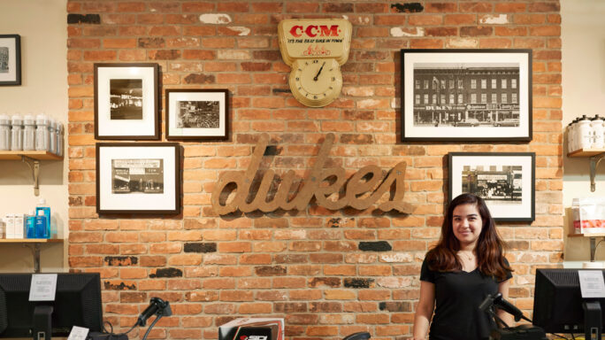 Woman in a black top sits at a desk in front of a red brick office wall with photos