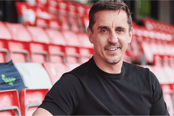   Gary Neville smiling sitting in a football stadium