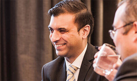 Ambitious looking businessman in a suit and tie smiling while his colleague drinks water from a glass