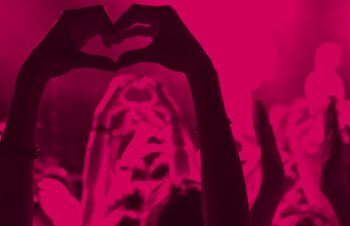 Photo of people with raised hands making heart shape at a concert