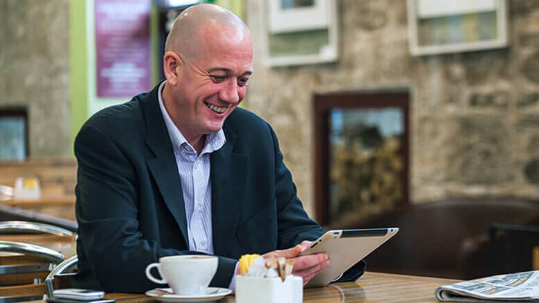 Smiling man wearing a suit and using a tablet at a café table