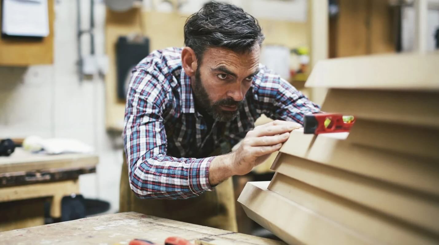  Person using a spirit level to check alignment on a wooden structure in a workshop