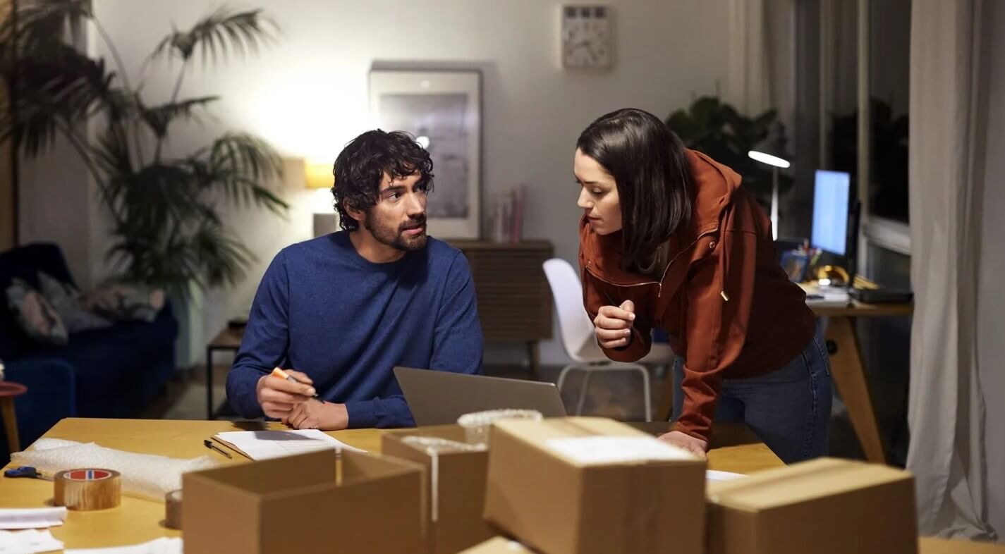 Two people reviewing notes and packages on a table in a home or office workspace