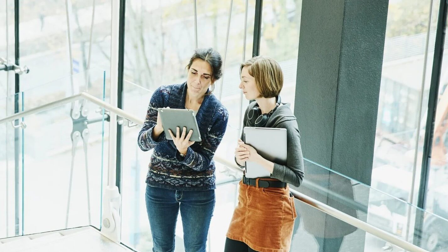  Two people walking through an office building while reviewing information on a tablet