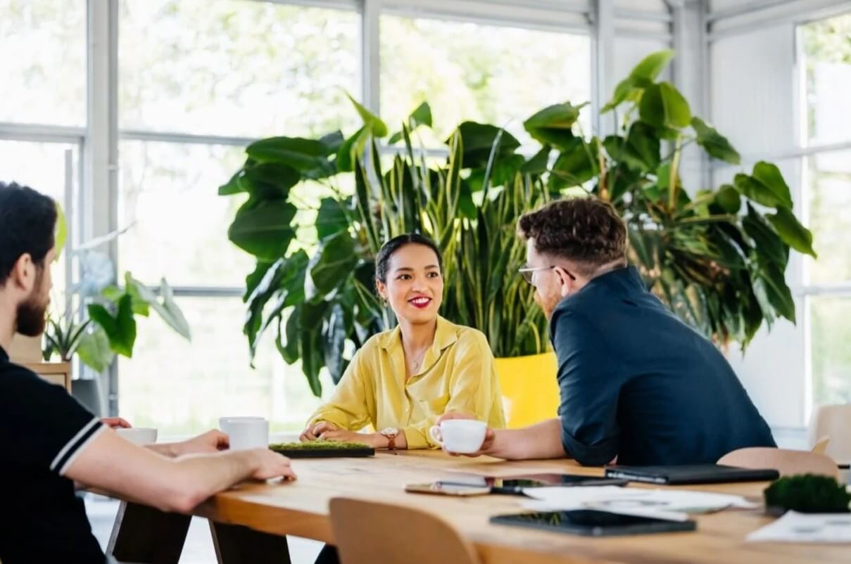  Three people meeting around a table in an office with laptops and notebooks