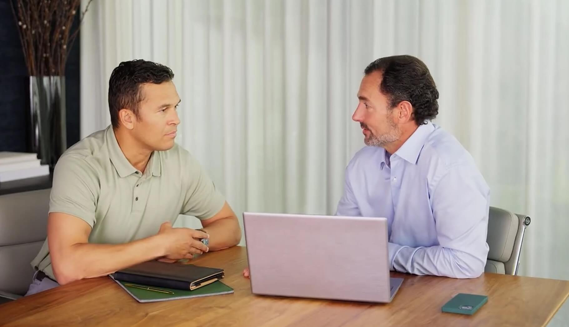  Two people seated at a table discussing work with a laptop and tablet