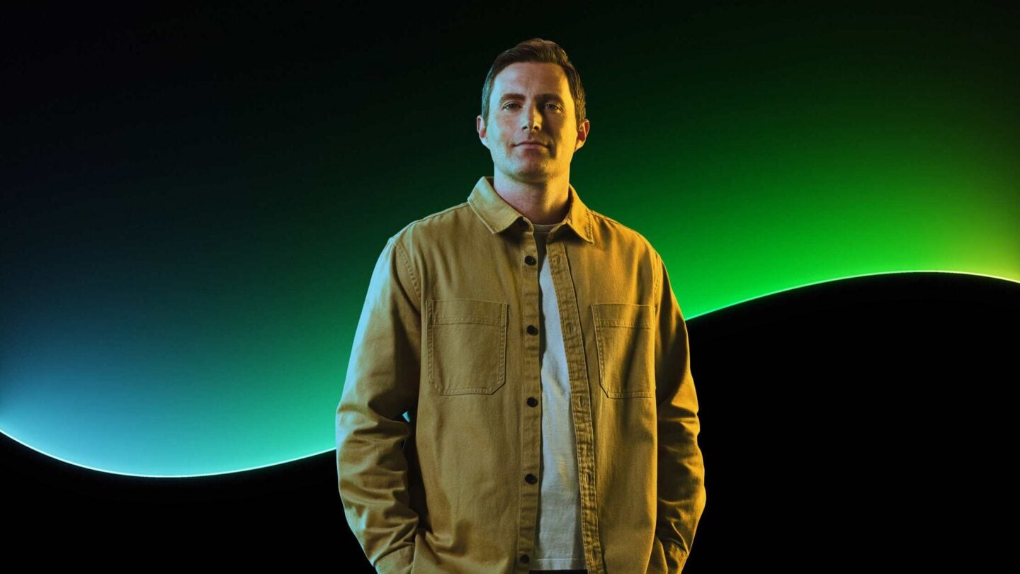 A man poses in front of the Sage glow line and a black background.