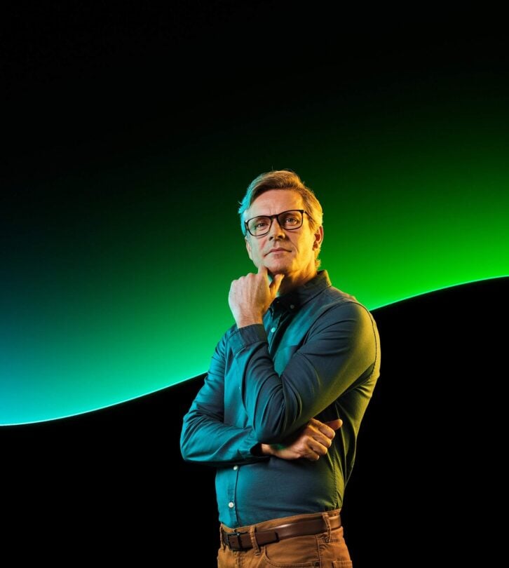 A man stands in front of the Sage glow line in front of a black background.