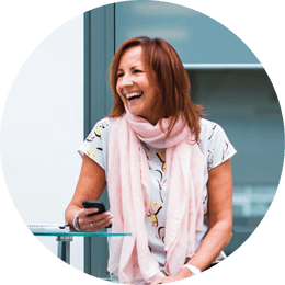 Roundel of an older woman with brown hair wearing a pink scarf laughing and holding a smartphone