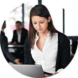 Roundel of a young woman with long dark hair wearing a white shirt and black sweater working on a laptop in an office