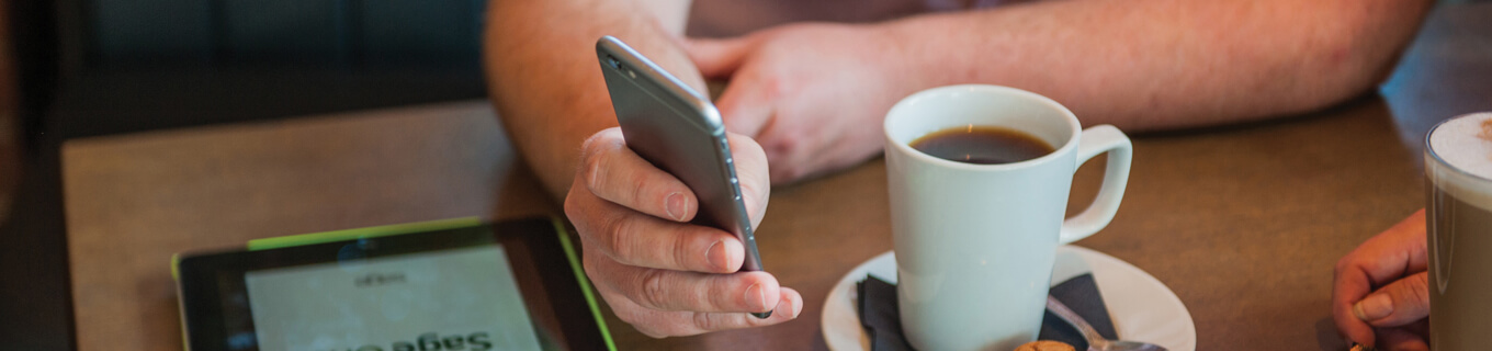 Man using a smartphone at a wooden table in a coffee shop