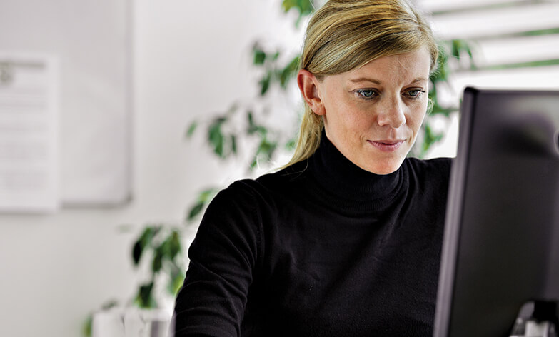 Businesswoman with blonde hair wearing a black turtleneck looking at a computer