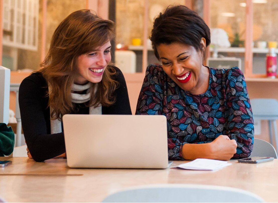 Two women smiling in front of a computer
