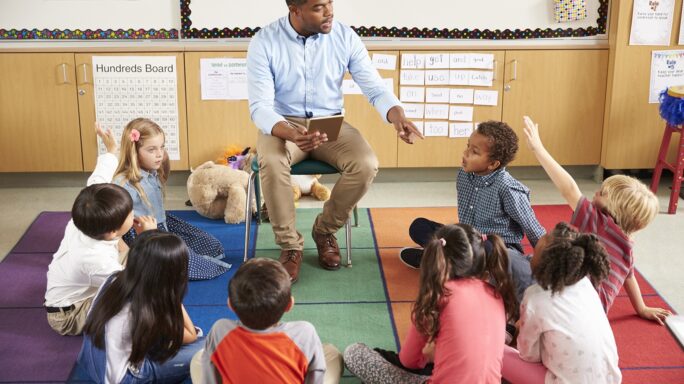 Adult black male teaching kids sitting at his feet