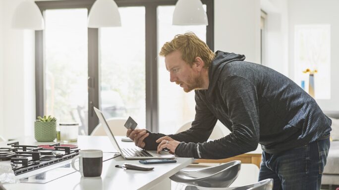 Middle-aged man holding credit card while operating computer