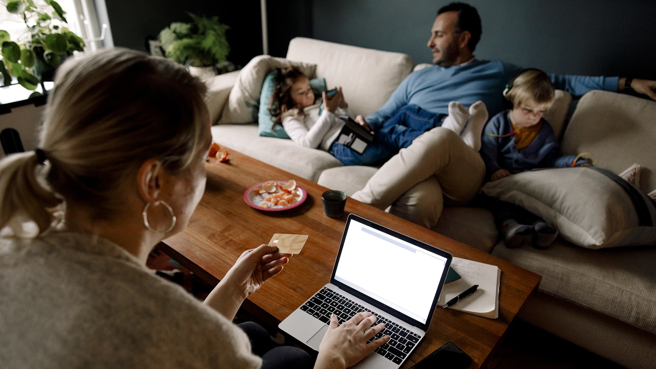 Woman inputting card details on laptop with man and child lying down on a couch
