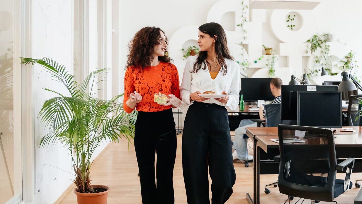 Two female co-workers talking with food in their hands