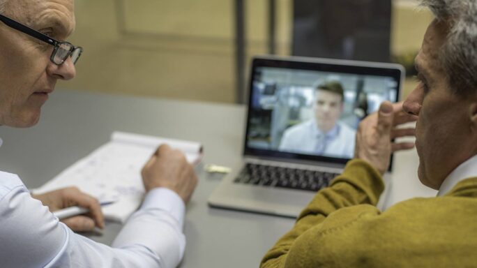 Two men having video conference with a colleague.