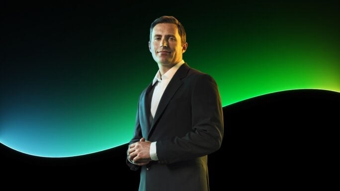 A man stands in front of the Sage glow line in front of a black background.