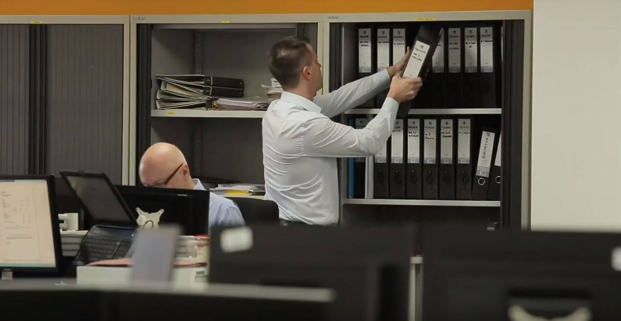 Hombre con ropa elegante que toma un archivo de una estantería en una oficina de aspecto convencional
