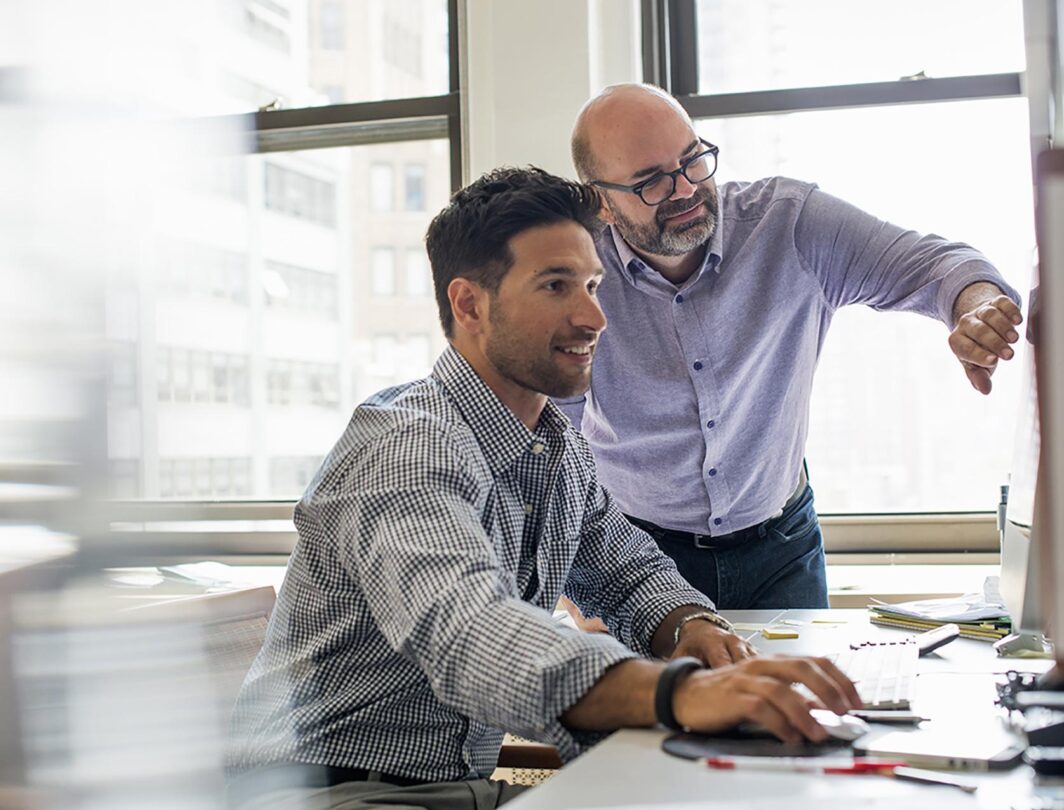 Deux hommes dans un office regardent un écran d'ordinateur en souriant