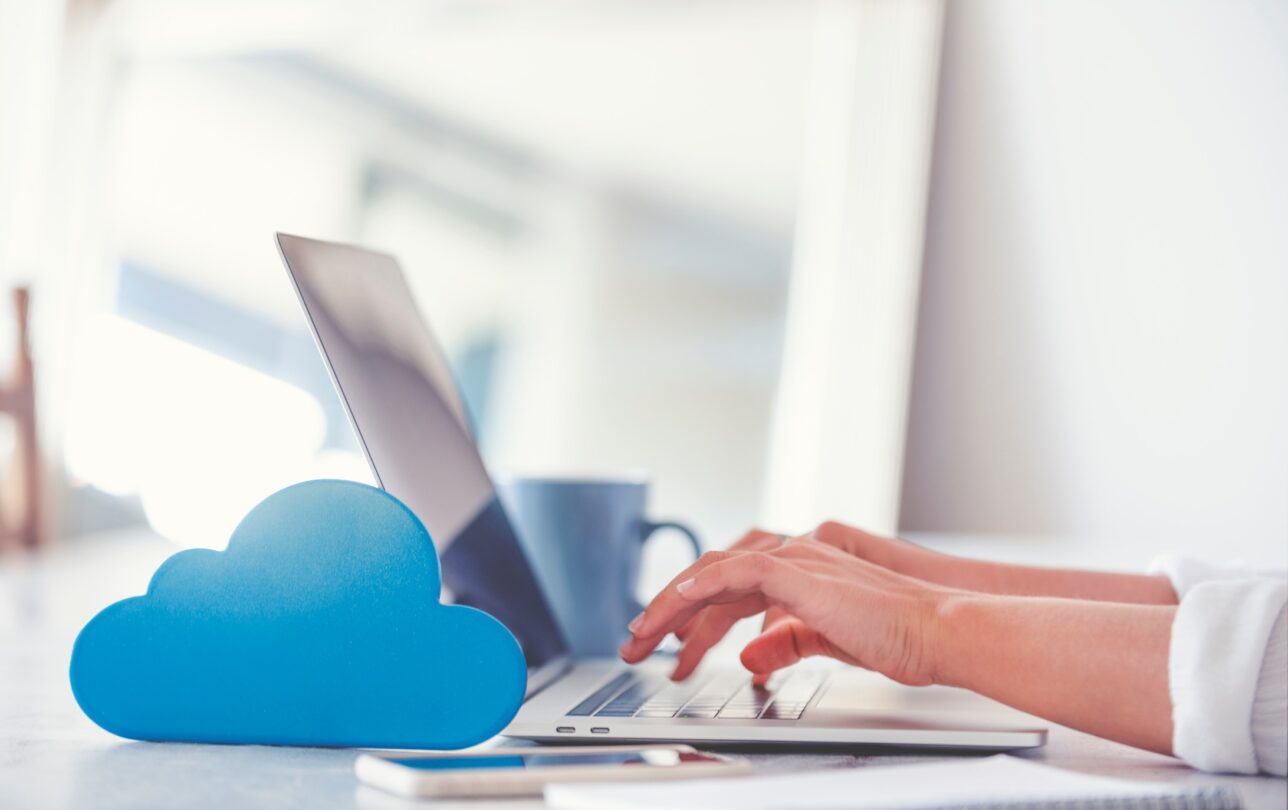 Une femme travaille sur son ordinateur portable. Il y a un symbole de nuage devant l'ordinateur, ce que signifique qu'elle travaille dans le cloud avec sa petite entreprise