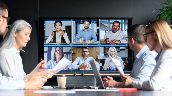 Le travail hybride : des collègues au bureau utilisent l'appel vidéo pour un meeting avec des collègues qui travaillent à leur domicile