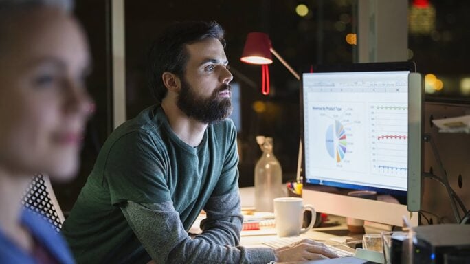 Op kantoor kijkt een man op zijn computerscherm, waar een dashboard met grafische rapporten op staat