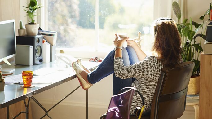 Een vrouw zit thuis achter haar bureau uit het raam te staren, te denken over hoe ze haar medewerkers kan motiveren