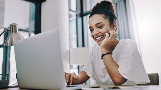 Een vrouw kijkt al lachend naar haar laptop en is geïnteresseerd in business intelligence
