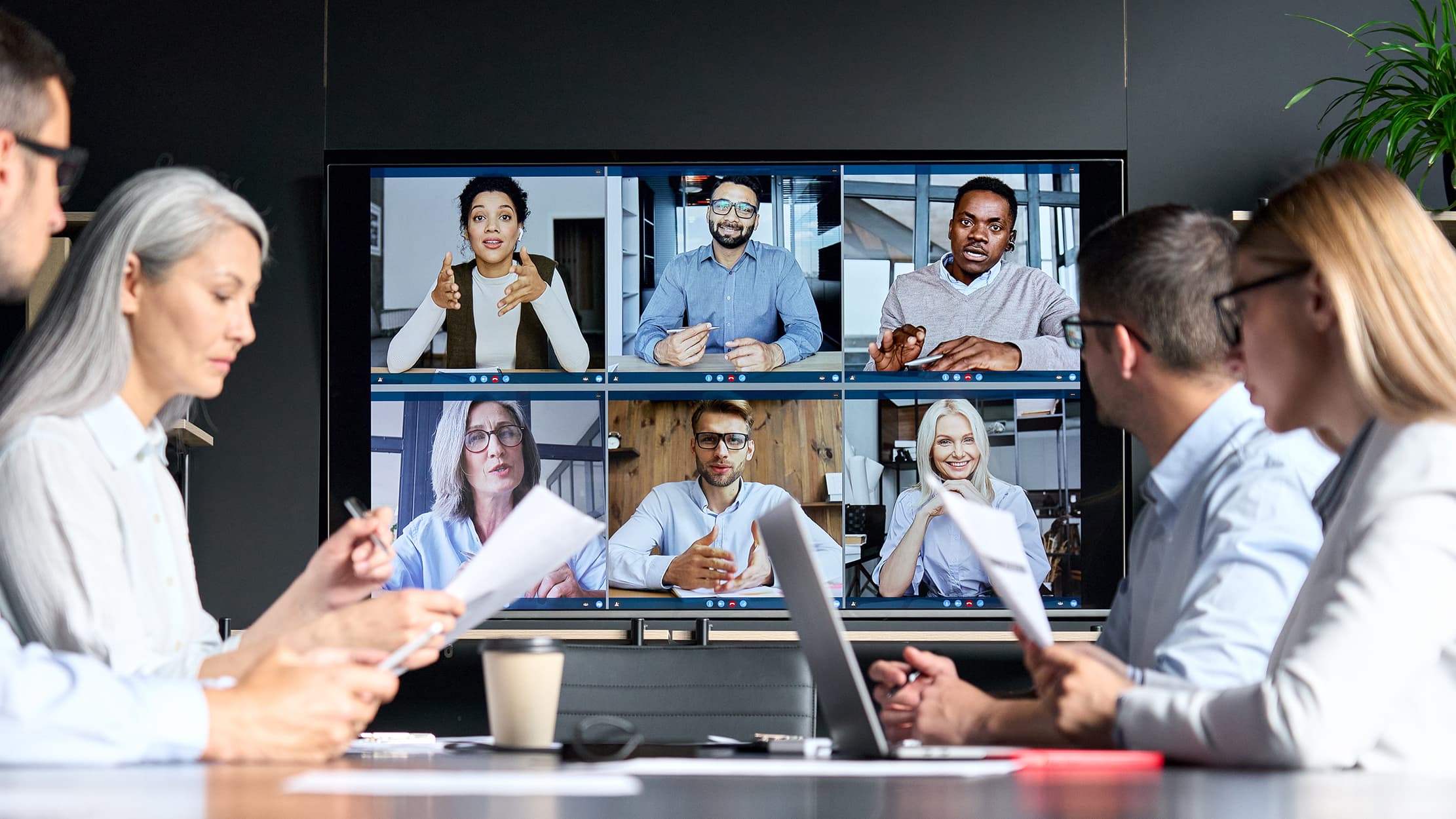Werknemers die aan hybride werken doen: collega's zitten op kantoor en videobellen met hun collega's die thuis werken